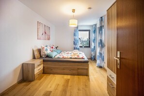 Een slaapkamer met een bed, een houten dressoir en een raam met gordijnen.