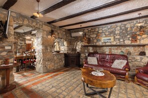 A stone-walled room with a wooden ceiling, a leather sofa, a wooden coffee table, and a dining area with chairs and a table. - Villa Cupido With Private Pool, Drivenik, Croatia (Drivenik)