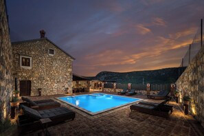 A stone building with a swimming pool, lounge chairs, and outdoor seating.