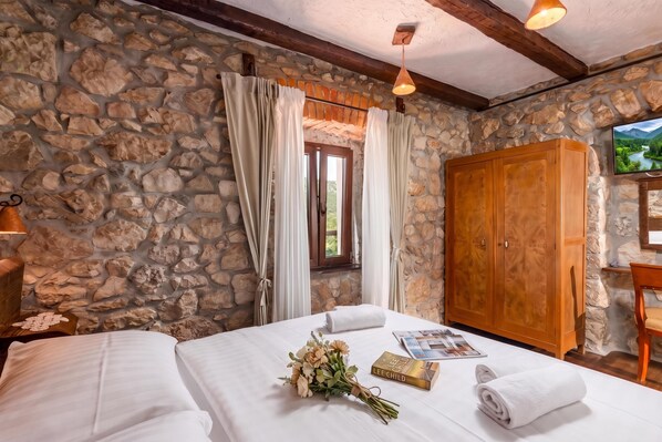 A bedroom with stone walls, a wooden wardrobe, a bed with white linens, a window with curtains, and a television on the wall. - Villa Cupido With Private Pool, Drivenik, Croatia (Drivenik)