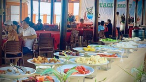 A restaurant with outdoor seating, multiple dining tables, and a variety of food dishes displayed on plates. - Peace Resort (Mui Ne)