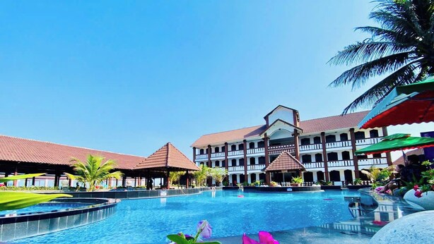 A swimming pool with a building in the background, surrounded by greenery and flowers. - Peace Resort (Mui Ne)