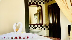 A hotel room with a bed, a heart-shaped towel decoration, a sink, and a mirror. - Peace Resort (Mui Ne)