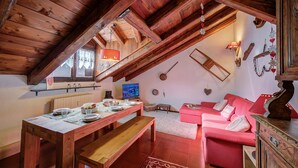 An attic room with a wooden ceiling, a dining table set with plates and glasses, a red sofa, and a television. - Le Meublè near the train station, close to Ski shuttle bus, Bardonecchia, Italy (Bardonecchia)