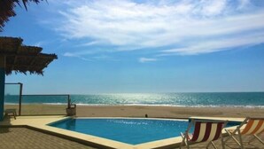A pool area with a view of the ocean, a thatched roof structure, and beach chairs. - COCOBOX (Los Organos)