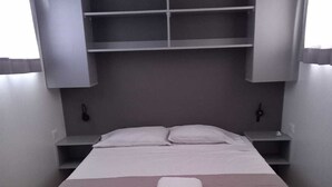 A neatly made bed with a folded towel, a bedside table with a lamp, and built-in shelving above the bed. - COCOBOX (Los Organos)