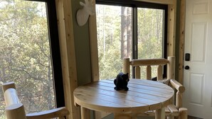 A wooden interior with a round table and chairs, a deer head decoration, and a view of trees through the window. - Family-sized, quaint cabin on the edge of the US Forest (Strawberry)