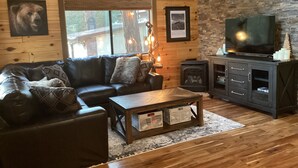 A cozy cabin interior with a leather sofa, a wooden coffee table, a fireplace, and a television. - Family-sized, quaint cabin on the edge of the US Forest (Strawberry)