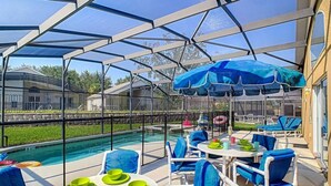Ein überdachter Außenbereich mit Pool, blauen Stühlen und Tischen mit grünen Tellern.