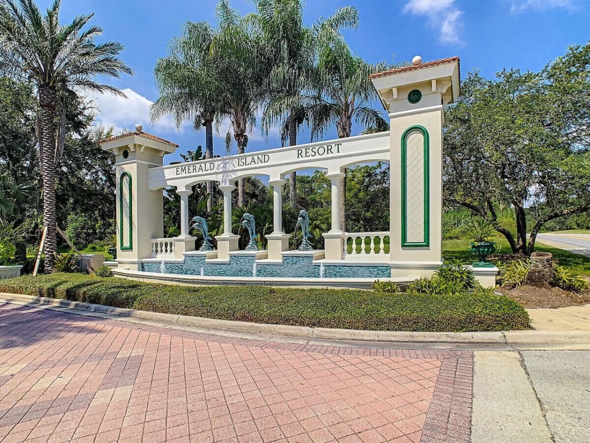 Entrada d'un centre vacacional amb un rètol que diu "Emerald Island Resort" i una font amb estàtues.