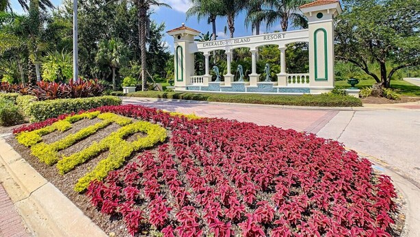 Eine angelegte Grünfläche mit einem zentralen Pavillon, auf dem "Emerald Island Resort" steht, umgeben von gepflegten Gärten mit roten und gelben Pflanzen.