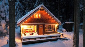 Eine Holzhütte mit einem mit Schnee bedeckten Deck und einem beleuchteten Innenraum.