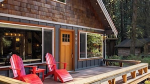 Eine Holzhütte mit einer Veranda, roten Adirondack-Stühlen und großen Fenstern.