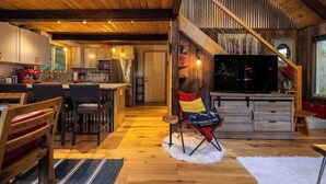 Ein großzügiger Wohnbereich mit Holzboden, ein Essbereich mit Stühlen, eine Küche mit Schränken und ein Fernseher im Wohnzimmer.