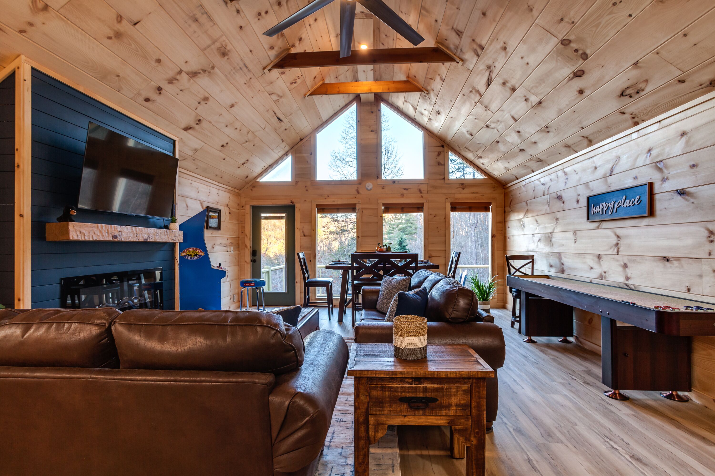 A cozy cabin interior with a fireplace, leather sofas, a pool table, and a TV mounted on the wall.