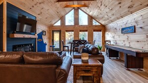Ein gemütliches Blockhauss-Interieur mit Kamin, Ledersofas, einem Billardtisch und einem an der Wand montierten Fernseher.