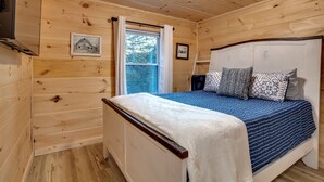 Ein Schlafzimmer einer Holzhütte mit einem Bett, einem Fenster mit Vorhängen und einem gerahmten Bild an der Wand.