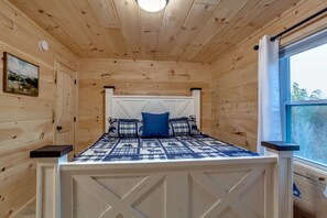 A wooden cabin bedroom with a bed, pillows, a painting, and a window. - Between Wears Valley & Pigeon Forge - Hot tub/views/grill/games (Sevierville)