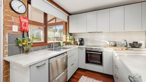 A modern kitchen with white cabinets, stainless steel appliances, and a brick wall. - A holiday home perfect for families seeking a peaceful getaway. (Lancelin)