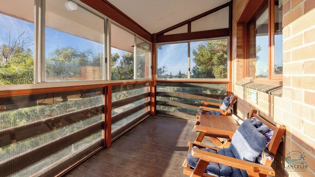 A covered outdoor seating area with wooden benches and cushions, large windows offering views of the surrounding landscape. - A holiday home perfect for families seeking a peaceful getaway. (Lancelin)