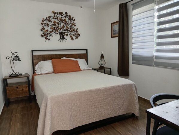 A bedroom with a bed, a nightstand, a lamp, a wall art piece, a window with blinds, and a chair.