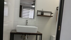 Kylpyhuone, jossa on valkoinen pesuallas, peili, pyyhe, wc-istuin ja roskakori.