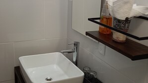Kylpyhuone, jossa on valkoinen pesuallas, peili ja hylly, jossa on hygieniatuotteita.