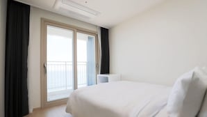 Ein Hotelzimmer mit Bett, Fenster mit Vorhängen, Klimaanlage an der Decke und einem kleinen Nachttisch.