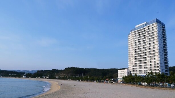 Ein hohes Hotel mit modernem Design in Strandnähe, der Himmel ist wolkenlos.