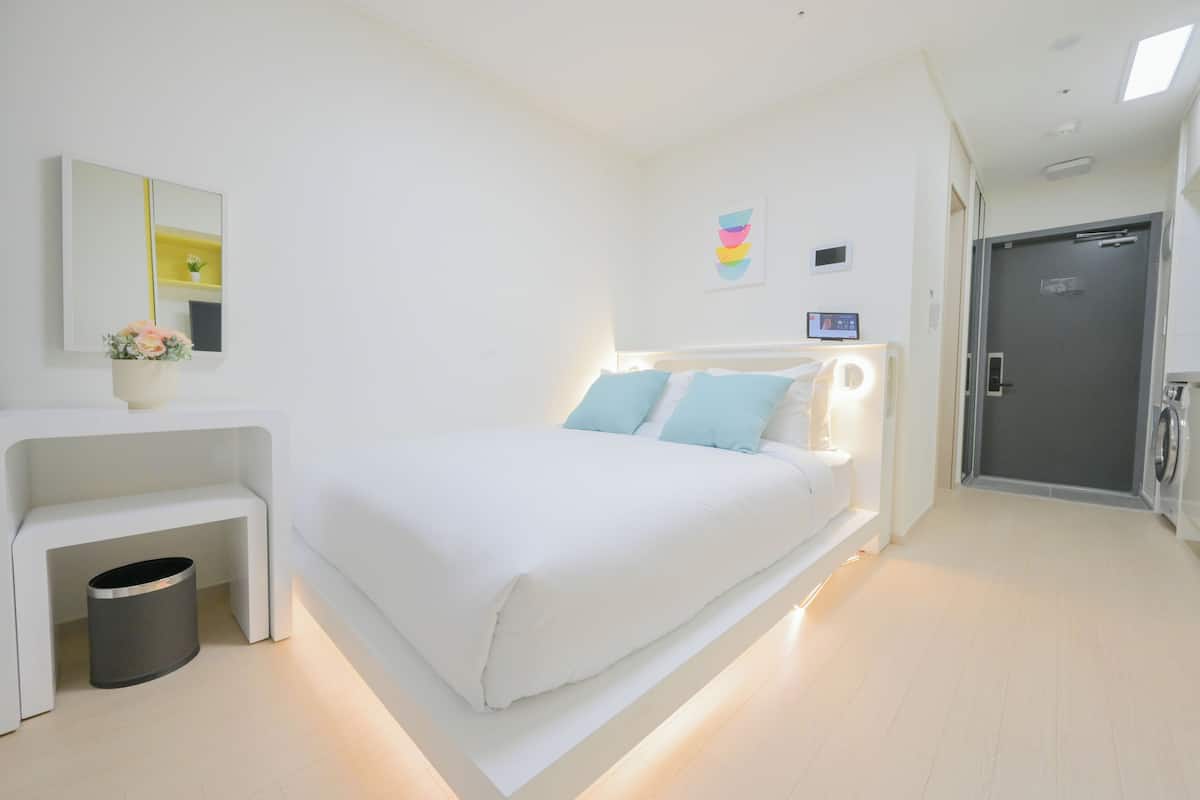 Une chambre d’hôtel moderne avec un grand lit, une table de chevet et une petite poubelle.
