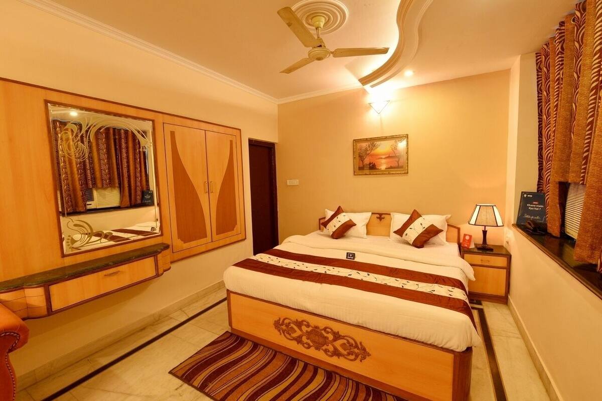 A bedroom with a bed, a ceiling fan, a nightstand, a lamp, a mirror, and a window with curtains.