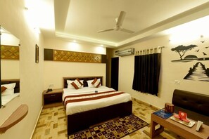 A hotel room with a bed, bedside table, nightstand, and a seating area with a sofa and a small table. - Hotel Mahima (Gwalior)