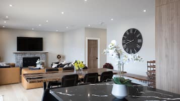 Uma sala de estar moderna com lareira, uma área de jantar com mesa de mármore e um relógio de parede grande.