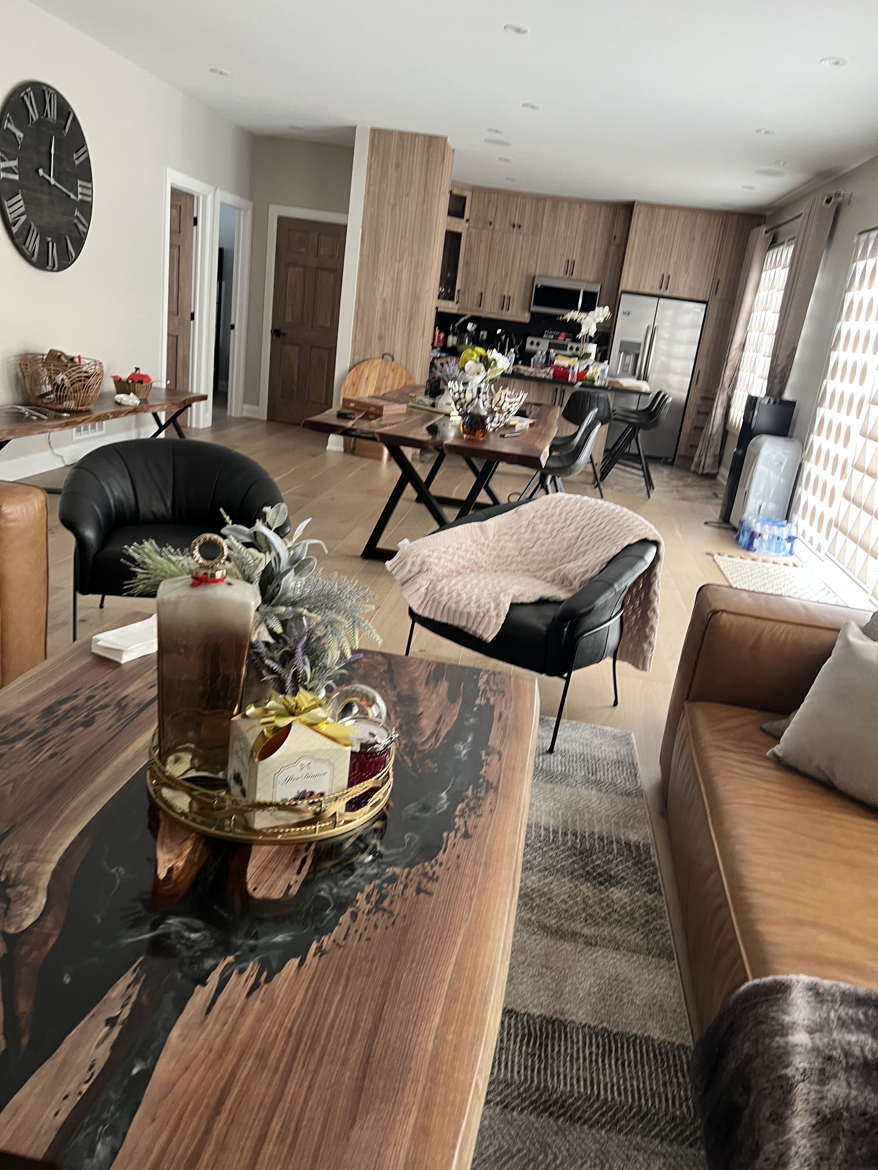 A modern living room with a dining area, featuring a wooden coffee table with a glass top, a black leather sofa, and a brown leather couch.