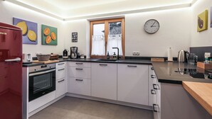 A modern kitchen with white cabinets, a red appliance, a clock, and artwork on the walls. - Vacation home for up to 10 people with 4 bedrooms, 210m², large garden (Inzell)