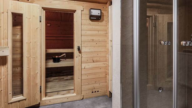 A wooden sauna with a glass door, a metal heater, and a small shelf with a pot. - Vacation home for up to 10 people with 4 bedrooms, 210m², large garden (Inzell)