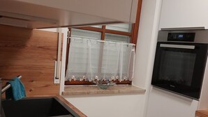 Een kleine keuken met een inbouwoven, een raam met bloemen gordijn en een houten aanrecht.