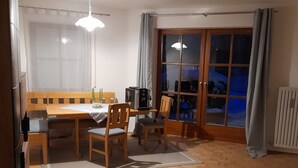 Een eethoek met een houten tafel en stoelen, een klein zwart apparaat, en een raam met gordijnen.