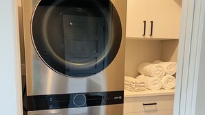 Une petite buanderie équipée de deux lave-linge à chargement frontal en acier inoxydable et d’un meuble blanc contenant des serviettes.