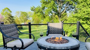 Une terrasse dotée de deux fauteuils en osier, d’une table ronde avec un foyer, et offrant une vue sur un paysage verdoyant.