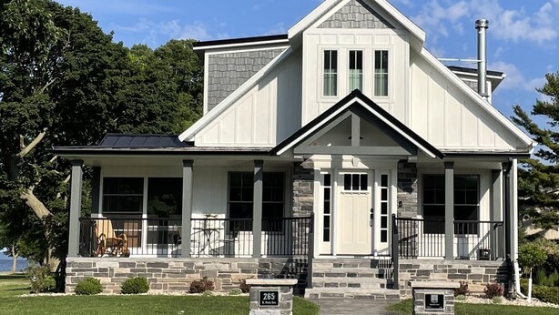 Une maison à deux étages, avec des fondations en pierre, un porche couvert et une allée menant à l’entrée.