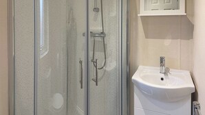 A bathroom with a glass-enclosed shower, a white sink, and a small cabinet with a mirror. - 1 bedroom accommodation in Kilwinning (Kilwinning)