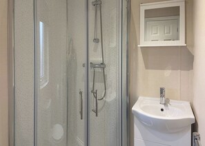 A bathroom with a glass-enclosed shower, a white sink, and a small cabinet with a mirror. - 1 bedroom accommodation in Kilwinning (Kilwinning)