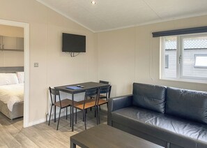 A room with a bed, a dining table with chairs, a leather sofa, a TV mounted on the wall, and a window with blinds. - 1 bedroom accommodation in Kilwinning (Kilwinning)