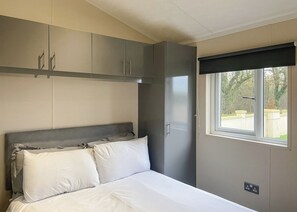 Et soveværelse med seng, gråt skab og et vindue med udsigt til grønne omgivelser.
