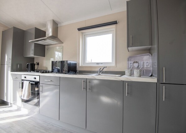 A modern kitchen with grey cabinets, a built-in oven, a microwave, and a coffee maker. - 1 bedroom accommodation in Kilwinning (Kilwinning)
