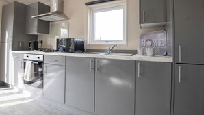 A modern kitchen with grey cabinets, a built-in oven, a microwave, and a coffee maker. - 1 bedroom accommodation in Kilwinning (Kilwinning)