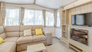 A living room with a sofa, a coffee table, a fireplace, and a television. - Spacious and luxurious 12ft-wide caravan with one double and one twin. (Axminster)