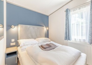 A neatly made bed with white linens, a bedside table with a lamp, and a window with curtains.