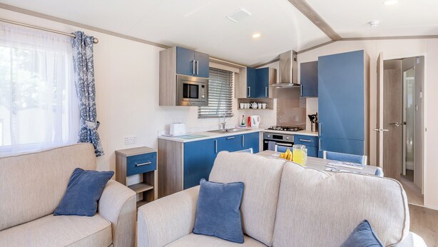 A compact living space with a kitchenette, a sofa, and a dining table. - Spacious and luxurious 12ft-wide caravan with one double and one twin. (Axminster)